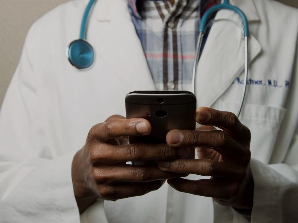 Un médico con un estetoscopio revisando mensajes en un teléfono