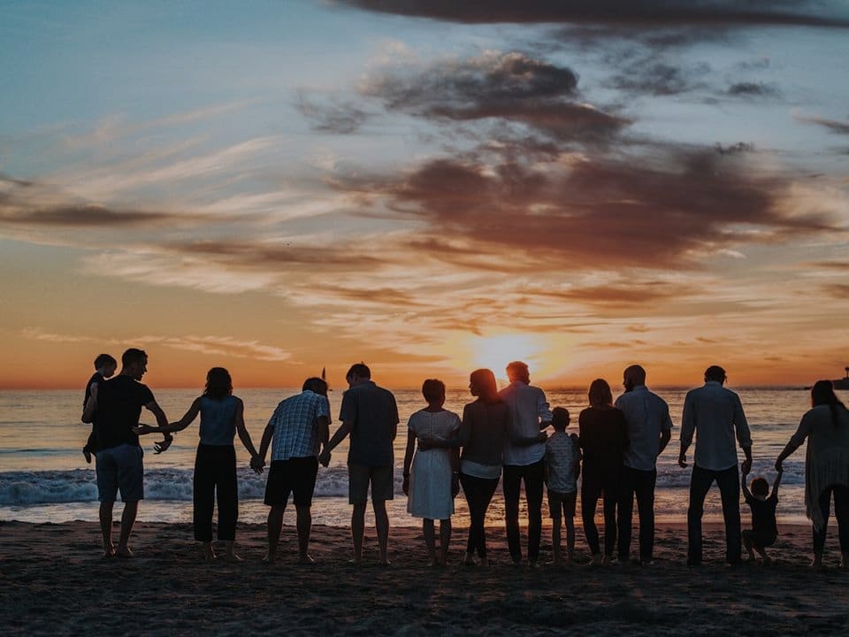 A multigenerational family holding hands on a beach at sunset