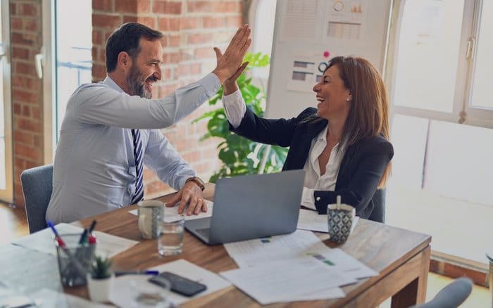 An advisor and client celebrating across a desk of paperwork